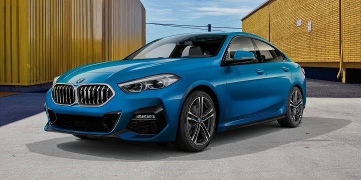 A blue metallic 2020 BMW 228i xDrive Gran Coupe parked between yellow buildings.