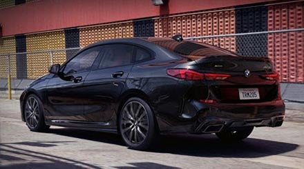 A black sapphire metallic BMW 2 Series Gran Coupe driving past a red and yellow building.